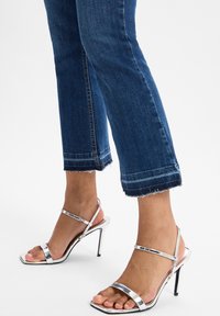 Sandali alti con tacco a stiletto argentati, con punta quadrata, caratterizzati da cinturini sottili e una finitura lucida. Abbinati a jeans croppati blu scuro.