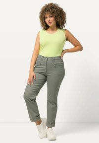 Ljusgrön ärmlös topp kombinerad med uppvikta olivgröna byxor med två fickor med dragkedja, kompletterad med vita sneakers.