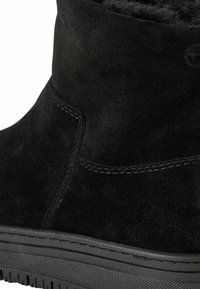 Fekete velúr bokacsizma textúrált felsőrésszel, sima varrással és mintázott gumitalppal. Puha bélés látható a felső szélen.