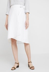 Vit linneinpackad kjol med rundad nederkant, med en knytning i midjan. Matchad med bruna sandaler med remmar. Slät textur.