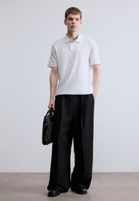 Fehér pólóing, fekete széles szárú nadrág és fekete bőr táska. Simább anyagok, klasszikus kialakítás és semleges színpaletta.