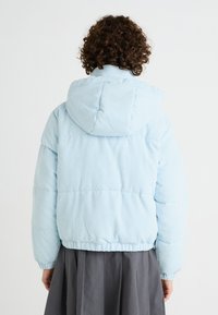 Světle modrá kordurová nafukovací bunda s kapucí a jemnou texturou, se zakončením na elastických manžetách a pase. Pohled zezadu ukazuje prošívaný design.