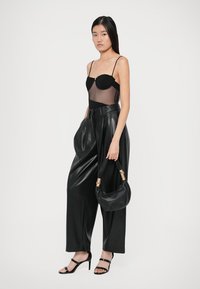 Body nera con pannelli in rete trasparente, pantaloni in pelle neri a vita alta e una piccola borsa nera con dettagli in oro. Sandali neri con strap.