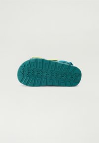 Teal gummisul med texturerad dragkraftsmönster och gula accenter. Rundade kanter och hållbar design lämplig för olika terränger.