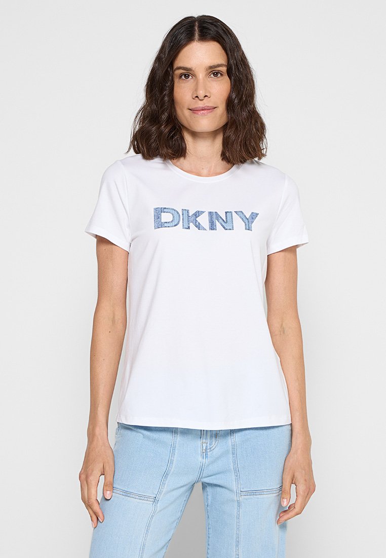 Camiseta blanca con un logo "DKNY" en denim azul. Mangas cortas, cuello redondo, corte estándar, textura suave y diseño casual.