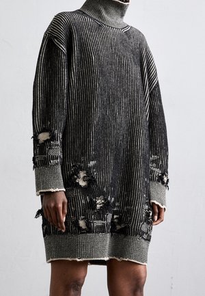 Robe en tricot rayée noir et blanc à manches longues avec col roulé, comportant plusieurs trous intentionnels et des détails usés sur les manches et l'ourlet.