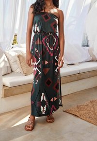 Abito maxi in tessuto verde scuro con motivi geometrici e tribali in bordeaux, bianco e rosa. Presenta una vita aderente e un design senza spalline.