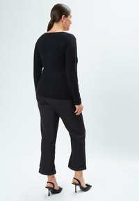 Schwarzer langer Pullover und schwarze Cropped-Hosen mit hochgekrempelten Säumen. Das Outfit besticht durch elegante Linien und minimalistisches Design. Schwarze High-Heels.