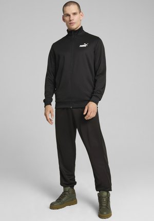 Svart zip-up träningsjacka med minimal vit logotyp, kombinerad med svarta tapered sweatpants och gröna hög-top sneakers. Strukturerad tyg.