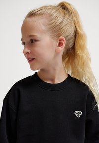 Svart sweatshirt med ribbad rundhals, med en liten broderad logotyp i vitt på vänster bröst. Slätt tyg, avslappnad passform.