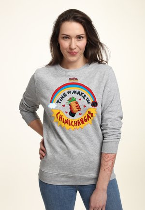 Kvinde iført grå sweatshirt med farverig tekst "Time to make the chimichangas" og tegnet hånd, der holder en burrito.