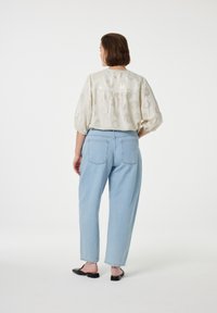 Leichte, gemusterte Bluse mit Puffärmeln und Yoke auf der Rückseite, kombiniert mit hellblauen High-Waist-Jeans. Schwarze flache Schuhe runden das Outfit ab.