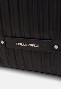 Czarna skórzana torba o karbowanej teksturze, z metalową srebrną tabliczką z logo "KARL LAGERFELD" i dwoma akcentami w srebrnym kolorze.