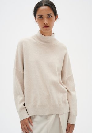 Pull à col roulé beige en matériau doux, à coupe décontractée, épaules tombantes et poignets côtelés. Design uni, sans motifs visibles.