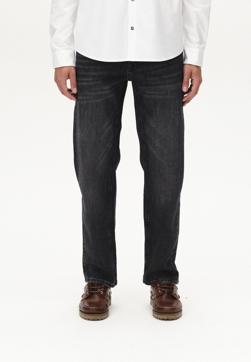 Jeans de denim oscuro con un diseño de pierna recta, que presentan un ligero desgaste y detalles de costura sutiles. Combinados con zapatos marrones con cordones.