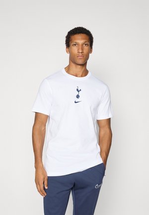 T-shirt en coton blanc présentant un logo bleu de Tottenham Hotspur et un swoosh bleu de Nike à l'avant. Manches courtes et col rond.