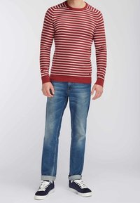 Maglione a righe rosse e bianche con scollo rotondo, abbinato a jeans in denim blu e sneakers blu navy, con maniche arrotolate.
