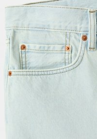 Jean en denim bleu clair en gros plan montrant la poche avant, la poche à monnaie avec rivets en cuivre, la passants de ceinture et les détails de couture jaunes.