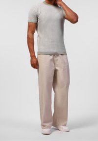 Maglietta a maniche corte a trama testurizzata grigio chiaro con bordi verdi, abbinata a pantaloni beige a gamba larga e sneakers bianche slip-on.