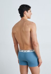 Boxer shorts de algodón azul con una cinturilla blanca que presenta el logo de Nike, mostrados en un modelo masculino desde un ángulo trasero.