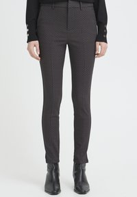 Tailored black patterned trousers with a fitted design, smooth fabric texture, and subtle geometric accents, paired with sleek ankle boots.