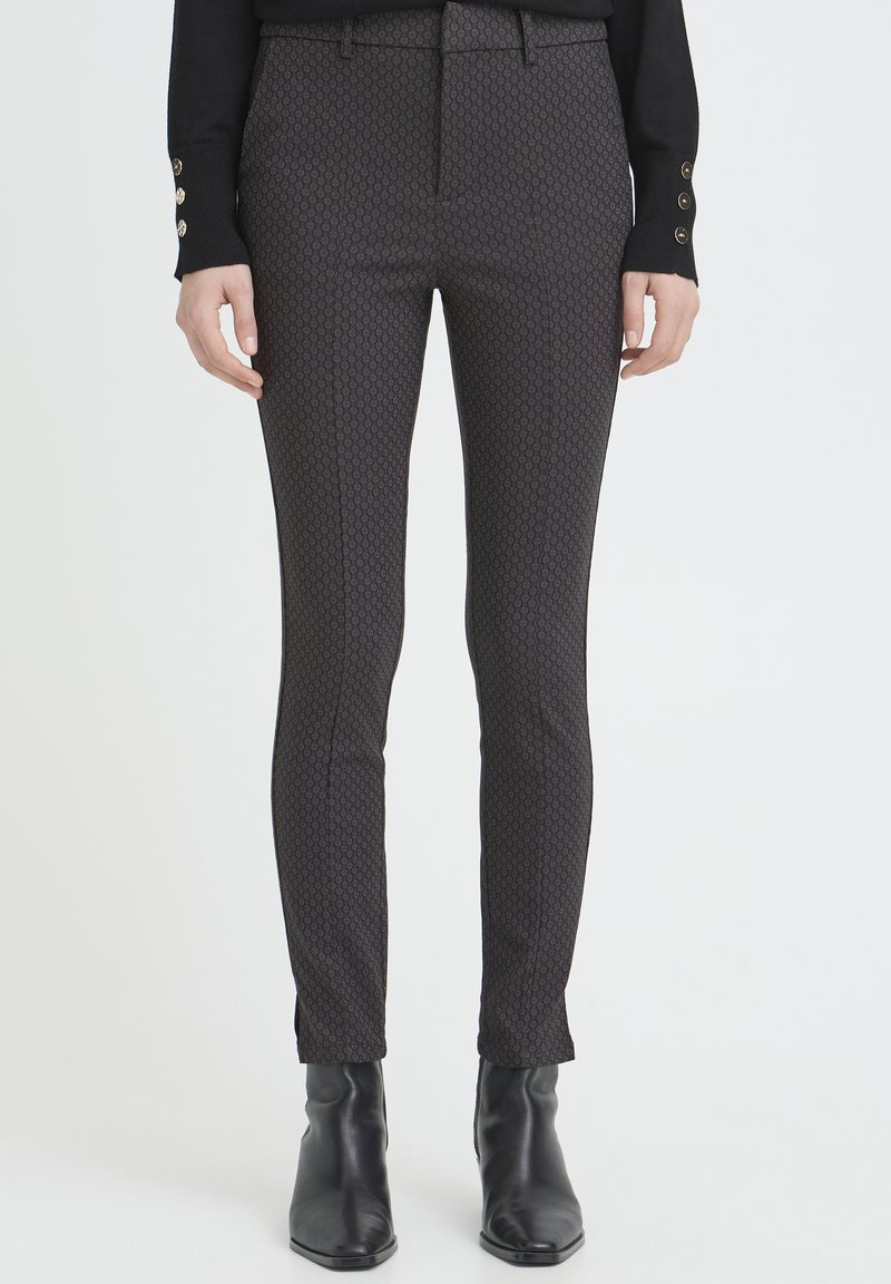 Tailored black patterned trousers with a fitted design, smooth fabric texture, and subtle geometric accents, paired with sleek ankle boots.