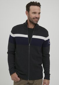 Pulover cu fermoar de culoare gri închis, dintr-un material texturat, având dungi orizontale albastre și albe pe piept și manșete ribbate.