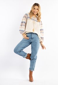 Blusa leggera con maniche a strisce blu e arancioni, abbinata a jeans in denim a vita alta e stivaletti alla caviglia color beige.