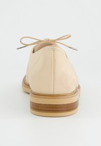 Beige kožená bota s kulatou špičkou, šněrovacím designem a nízkým dřevěným podpatkem. Disponuje minimálním prošíváním pro čistý vzhled.