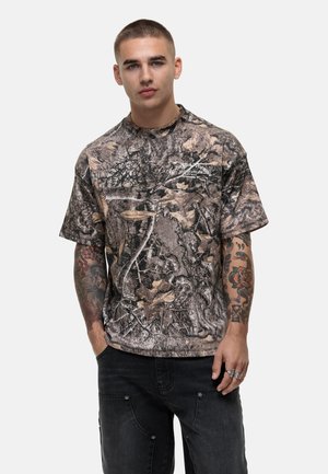Korte mouw shirt met camouflagepatroon in aardetinten en bladerontwerpen. Heeft een ronde hals en een relaxte pasvorm. Accentlogo op de borst.