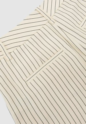 Beige nadrág közeli képe vékony, függőleges fekete csíkokkal, övbújtatókkal és hátsó paszpólos zsebbel.