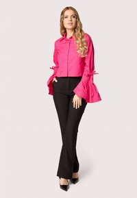 Camicia rosa a maniche flared e con laccetti, abbinata a pantaloni neri attillati e tacchi a punta neri.
