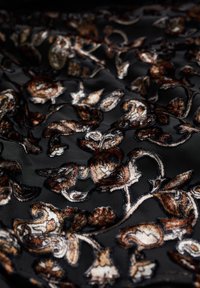 Tissu noir avec des motifs floraux et cachemire brodés en marron brillant, or et argent, créant une surface texturée.