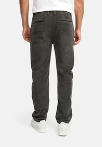 Dark gray corduroy pants with vertical ribbing, two back pockets, and a straight leg cut, worn with white sneakers.