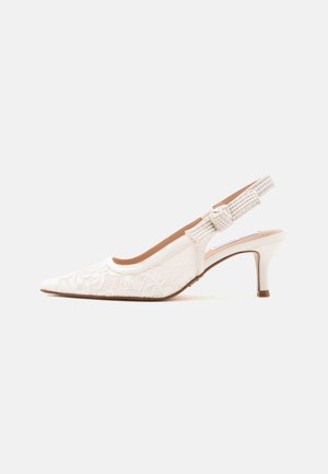 Scarpa slingback bianca in pizzo con punta affusolata, tacco sottile di media altezza e cinturino testurizzato con dettaglio a fiocco.