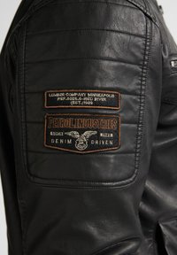 Chaqueta de cuero negra con textura acolchada, detalles cosidos y parches bordados de Petrol Industries y Lumber Company Minneapolis.