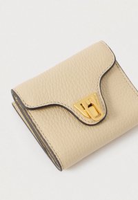 Μπεζ υφασμάτινο δερμάτινο πορτοφόλι με κυματιστό καπάκι και χρυσή ορθογώνια πόρπη σε λευκό φόντο.