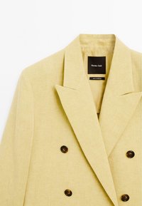 Hellgelbe, doppelt gefüllte Blazerjacke mit Spitzrevers und dunklen Knöpfen, ausgestattet mit einem Etikett innen, auf dem "Massimo Dutti" steht.