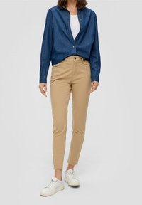 Jeansknappad skjorta i mörkblå, tillsammans med ljusbruna, åtsittande byxor och vita sneakers. Outfiten har en avslappnad passform och en stilren design.