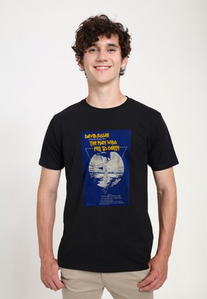 Sort bomulds T-shirt med et blåt grafisk tryk af en filmplakat med hvid og gul tekst, der viser David Bowie i "Manden der faldt til jorden."