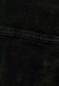 Tessuto denim nero con una texture liscia e una leggera lucentezza, caratterizzato da un dettaglio della cucitura che corre orizzontalmente attraverso il materiale.