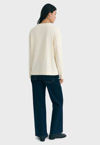 Long-sleeve cream sweater with a relaxed fit, paired with dark wide-leg jeans. The knit texture is visible, with simple silhouette and no designs.