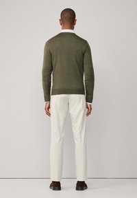 Olive green knitted sweater with a ribbed hem, paired with light beige trousers. The outfit features a subtle texture and clean lines.
