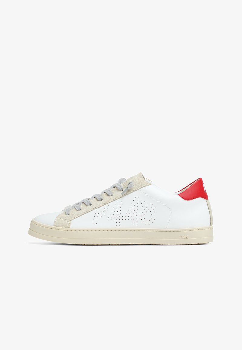 Baskets basses blanches avec des accents en daim beige, des lacets gris, un logo perforé sur le côté, une semelle beige et un onglet de talon rouge avec texte blanc.