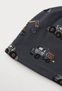Cappello lavorato a maglia di colore grigio scuro con motivi di camion ed escavatori. Presenta una texture morbida e una vestibilità aderente, ideale per un look casual o per attività all'aperto.