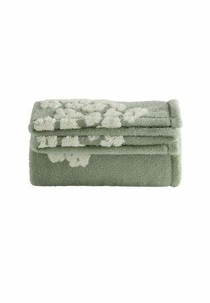 Couverture pliée douce verte avec des motifs floraux blancs en relief sur un tissu à texture lisse sur fond blanc.