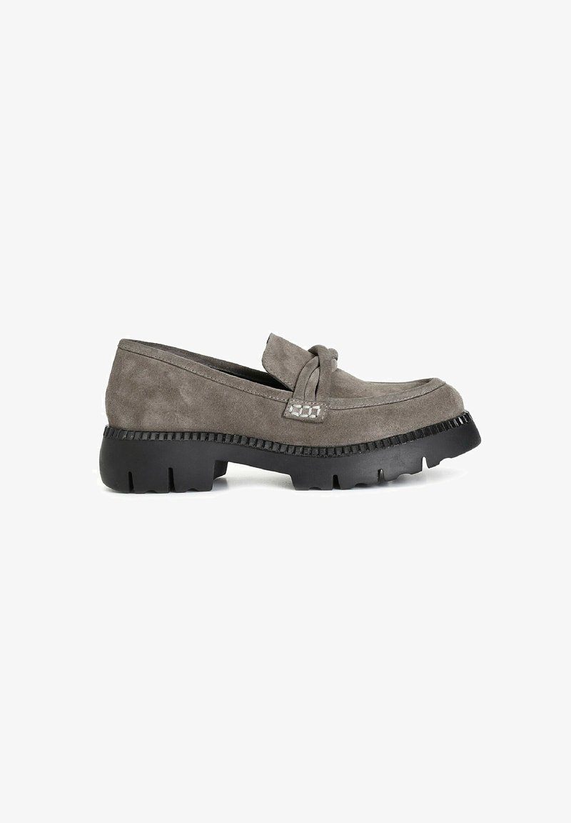Mocasines de ante gris con un detalle anudado en la lengüeta, suela de goma negra gruesa y borde texturizado. Vista lateral que muestra el diseño y la forma.