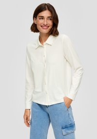 Witte blouse met lange mouwen en kraag, voorzien van een knoopsluiting aan de voorkant en een soepele textuur, gecombineerd met lichtblauwe jeans.