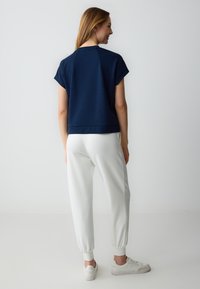 Top blu navy a maniche corte con vestibilità comoda, abbinato a pantaloni jogger bianchi con polsini elasticizzati e una superficie liscia.