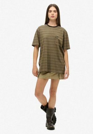 T-shirt w zielone paski w kolorze oliwkowym z krótkimi rękawami i kieszonką na piersi, zestawiony z krótką spódnicą w kolorze khaki i czarnymi bootami do kolan.